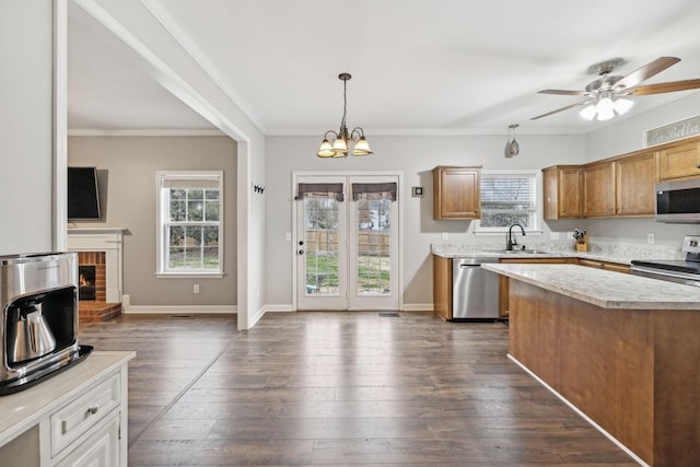 kitchen with appliances with stainless steel finishes, hanging light fixtures, sink, dark hardwood / wood-style floors, and a brick fireplace