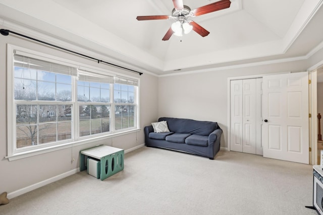 living area with a raised ceiling, light carpet, and ceiling fan