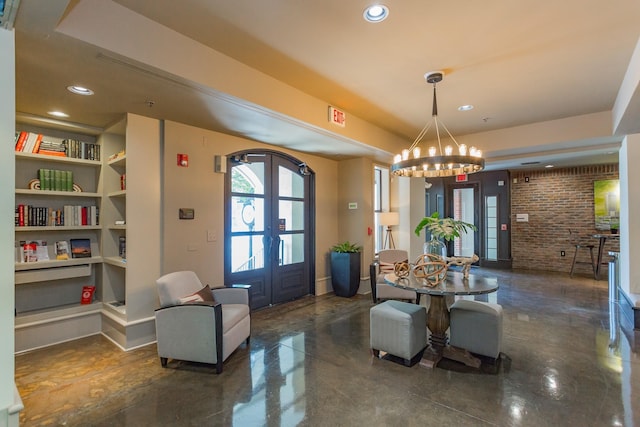 interior space with french doors, an inviting chandelier, brick wall, and a raised ceiling