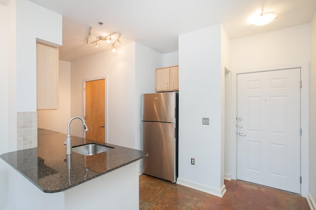 kitchen featuring dark stone countertops, sink, kitchen peninsula, and stainless steel fridge