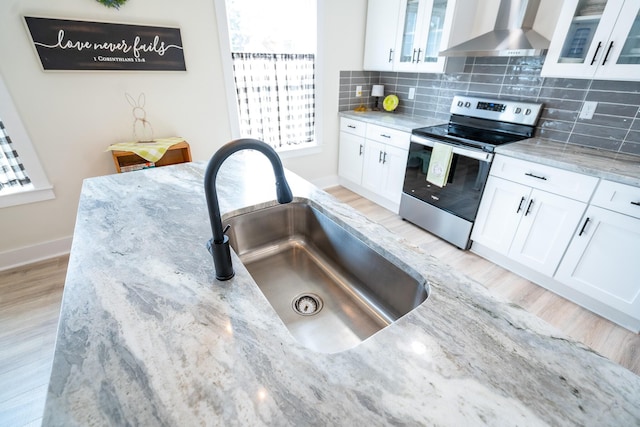 kitchen with white cabinets, electric stove, light stone countertops, and wall chimney exhaust hood