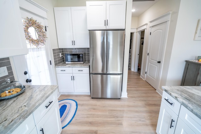 kitchen featuring white cabinetry, light wood-type flooring, light stone countertops, and stainless steel appliances