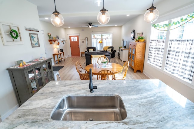 kitchen featuring sink, light stone counters, hanging light fixtures, and light hardwood / wood-style floors