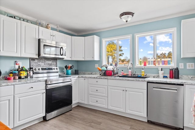 kitchen featuring light wood-type flooring, light stone countertops, sink, appliances with stainless steel finishes, and white cabinets