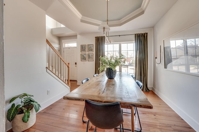 dining room featuring a raised ceiling, ornamental molding, and light wood finished floors