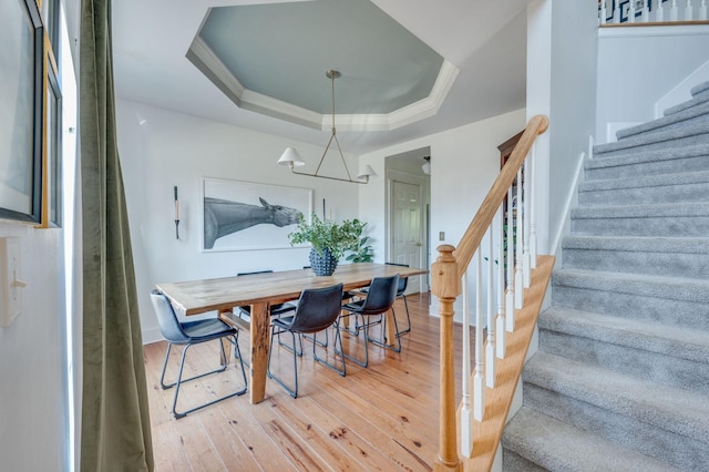 dining space with wood finished floors, a raised ceiling, crown molding, and stairs