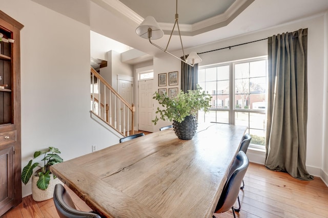 dining area featuring ornamental molding, stairs, light wood-style floors, and a tray ceiling