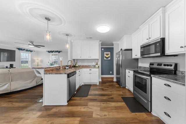 kitchen with appliances with stainless steel finishes, a breakfast bar area, white cabinets, decorative light fixtures, and kitchen peninsula