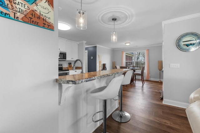 kitchen featuring white cabinetry, hanging light fixtures, stainless steel appliances, crown molding, and a breakfast bar area