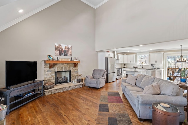 living room featuring a notable chandelier, a stone fireplace, a towering ceiling, light hardwood / wood-style floors, and crown molding