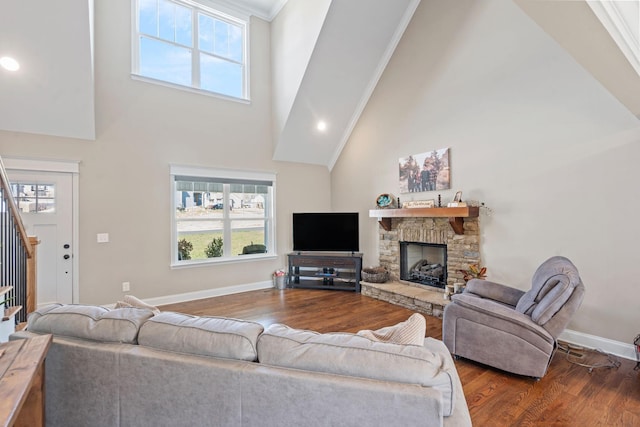 living room with high vaulted ceiling, a stone fireplace, crown molding, and wood-type flooring