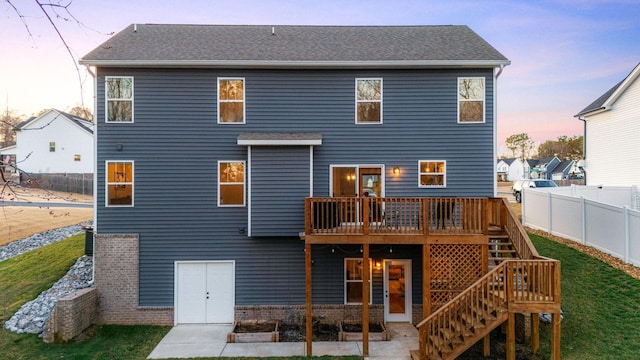 back house at dusk featuring a wooden deck and a lawn