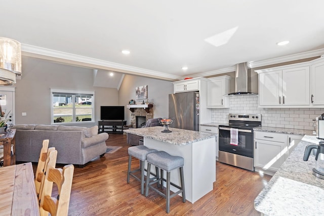 kitchen featuring white cabinetry, a center island, light stone countertops, appliances with stainless steel finishes, and wall chimney exhaust hood