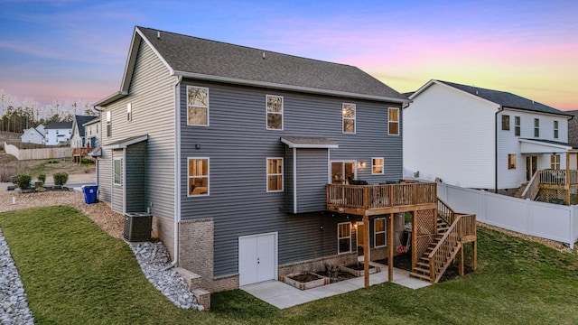 back house at dusk featuring a wooden deck, cooling unit, and a lawn