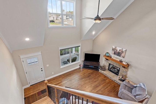 foyer with hardwood / wood-style flooring, a towering ceiling, a stone fireplace, ornamental molding, and ceiling fan