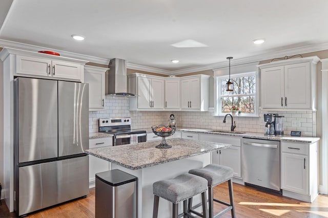 kitchen with wall chimney exhaust hood, stainless steel appliances, white cabinets, a kitchen island, and sink