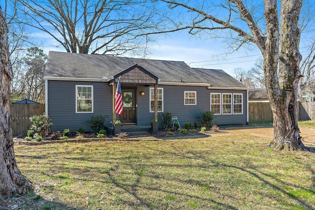 view of front of house with roof with shingles, a front yard, and fence