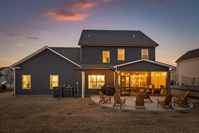 back house at dusk featuring a lawn, a patio, and central AC unit