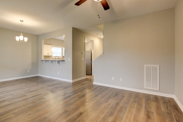 unfurnished living room featuring ceiling fan with notable chandelier, baseboards, visible vents, and wood finished floors