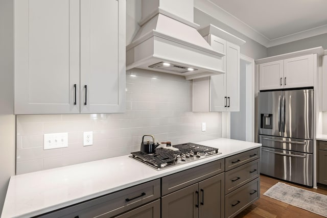 kitchen with light countertops, appliances with stainless steel finishes, white cabinetry, tasteful backsplash, and custom exhaust hood