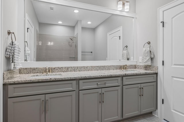 bathroom featuring a sink, a tile shower, double vanity, and visible vents