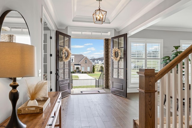 entrance foyer with a wealth of natural light, ornamental molding, wood finished floors, and a tray ceiling