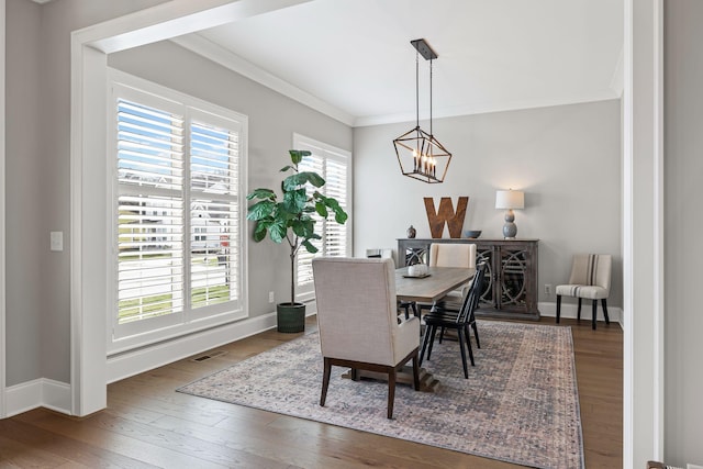 dining room with dark wood-style floors, a healthy amount of sunlight, ornamental molding, and a chandelier
