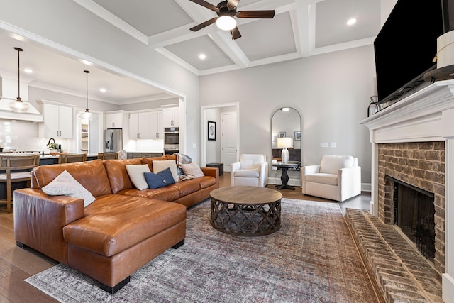 living area with a ceiling fan, dark wood finished floors, coffered ceiling, a fireplace, and beamed ceiling