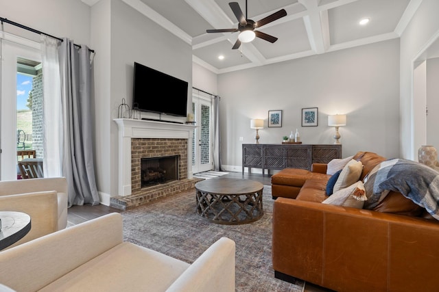 living area with a ceiling fan, baseboards, a brick fireplace, coffered ceiling, and beamed ceiling