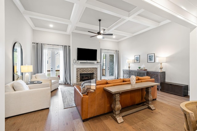 living room with ceiling fan, coffered ceiling, beamed ceiling, light wood-type flooring, and a fireplace