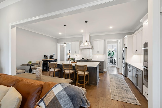 kitchen with appliances with stainless steel finishes, a center island with sink, light countertops, decorative light fixtures, and white cabinetry