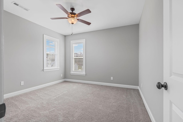 spare room featuring light colored carpet, ceiling fan, visible vents, and baseboards