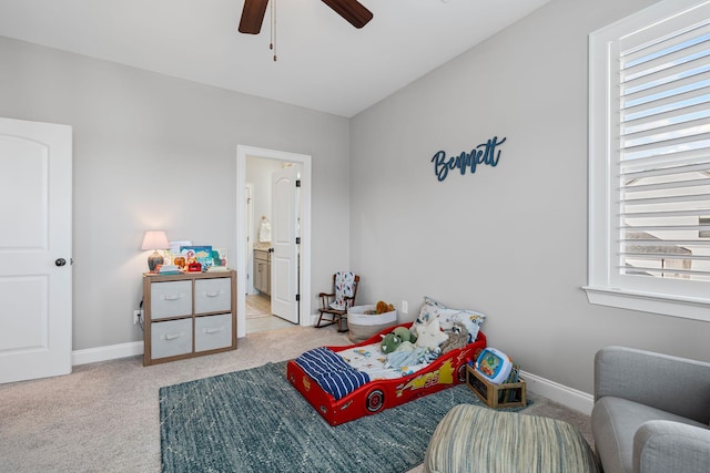 bedroom featuring baseboards, ensuite bath, light colored carpet, and ceiling fan