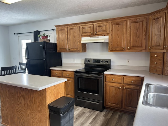 kitchen featuring light countertops, brown cabinetry, under cabinet range hood, and black appliances