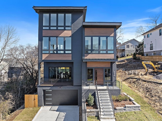 modern home featuring stairway, an attached garage, fence, driveway, and brick siding