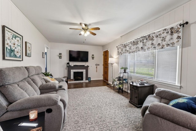 living area with a brick fireplace, a ceiling fan, and wood finished floors