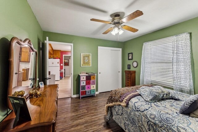 bedroom with freestanding refrigerator, ceiling fan, baseboards, dark wood finished floors, and a closet