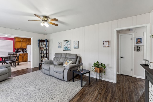 living room featuring baseboards, ceiling fan, and dark wood-style floors