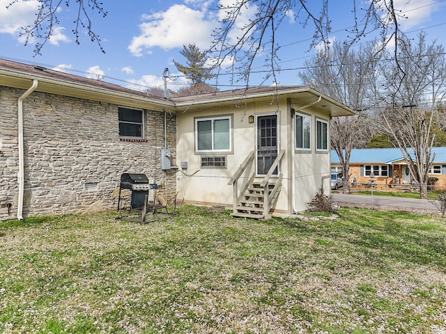 rear view of house with stucco siding, entry steps, a yard, and stone siding