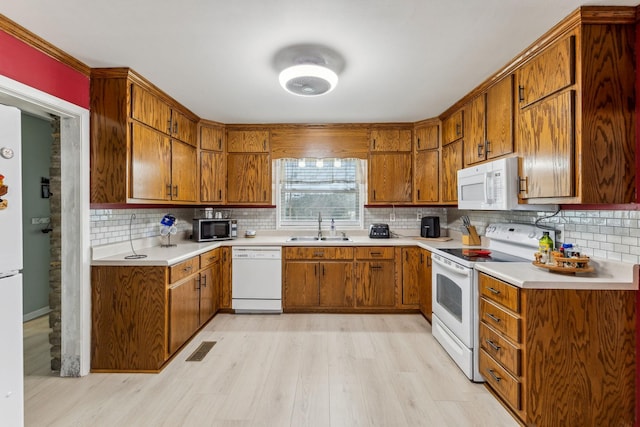 kitchen with light wood finished floors, brown cabinets, a sink, light countertops, and white appliances