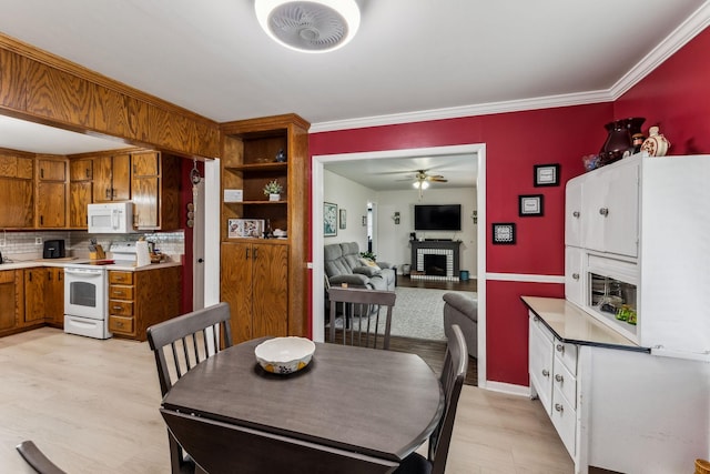 dining space featuring crown molding, a ceiling fan, a brick fireplace, and light wood-style floors