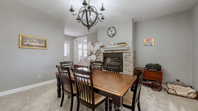 dining room with baseboards, a stone fireplace, light carpet, and a chandelier