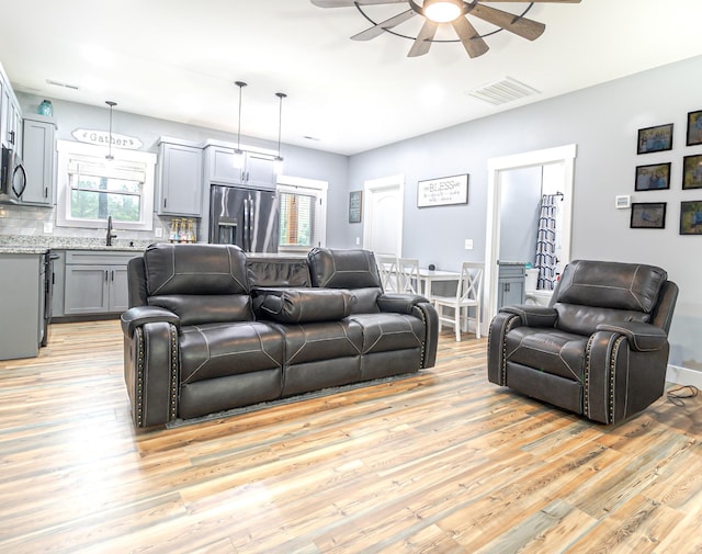 living room with baseboards, ceiling fan, visible vents, and light wood-type flooring