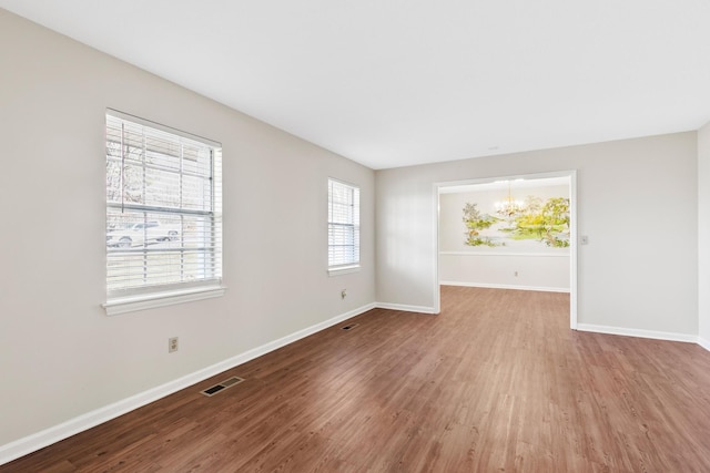 empty room featuring a notable chandelier, visible vents, baseboards, and wood finished floors