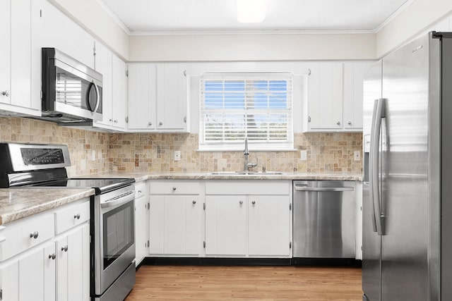 kitchen featuring a sink, ornamental molding, appliances with stainless steel finishes, light wood finished floors, and white cabinets