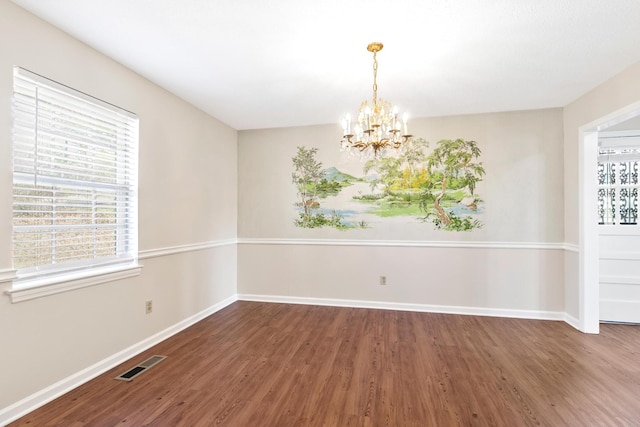 empty room with baseboards, visible vents, a chandelier, and wood finished floors