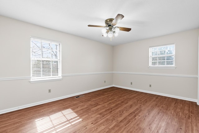 empty room with a healthy amount of sunlight, baseboards, visible vents, and wood finished floors