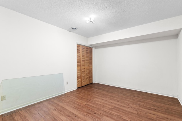 spare room featuring baseboards, visible vents, a textured ceiling, and wood finished floors