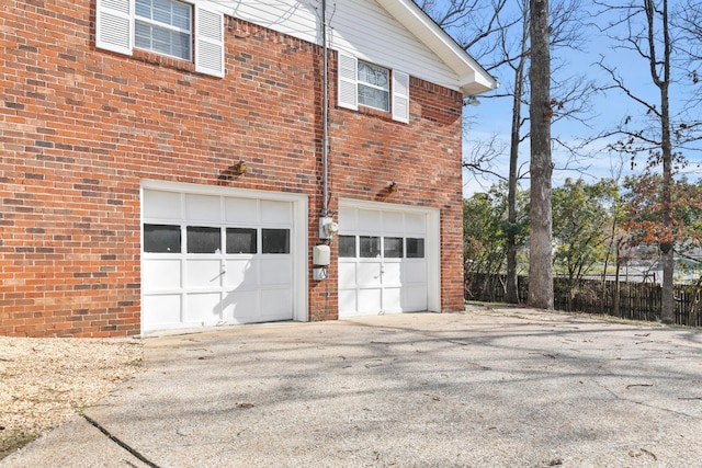 view of property exterior featuring fence, driveway, a garage, and brick siding