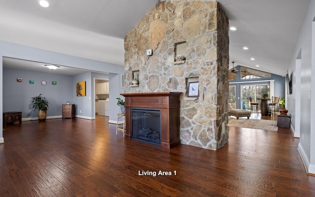 unfurnished living room with wood finished floors, a stone fireplace, baseboards, lofted ceiling, and washer / clothes dryer